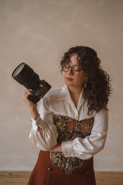 woman sits on stool holding a camera smiling