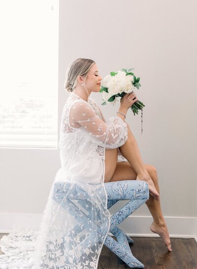 Bride sitting in her getting ready attire while holding her flowers and smelling them