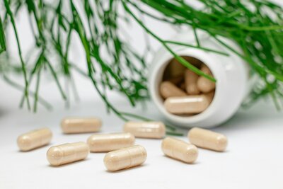 Supplement capsules spilling out of a bottle next to plant leaves