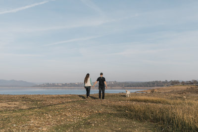 man and woman walking with dog next to lake