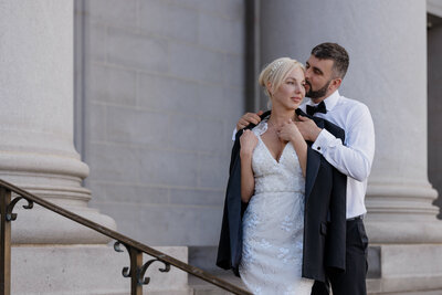 Groom puts jacket over bride's shoulder during Denver courthouse elopement.