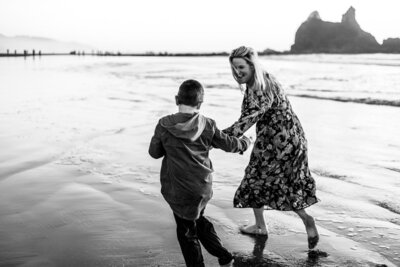 Black and white image of mom and son running on beach.