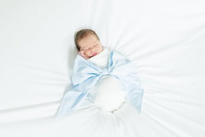 newborn baby boy laying on bed wrapped in Beaufort Bonnet Company bow swaddle