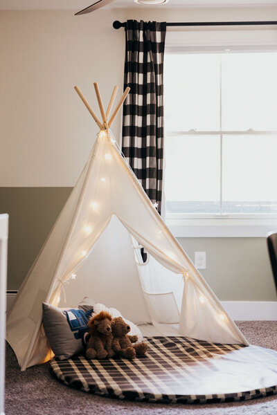 A child's play tent with stuffed animals in front of an open window with checkered curtains.