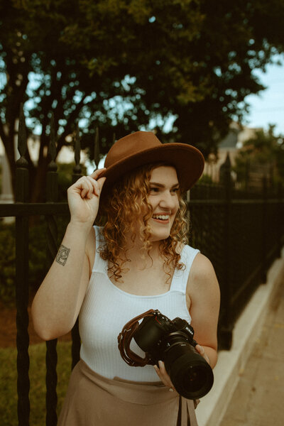 woman holding camera and tipping her hat