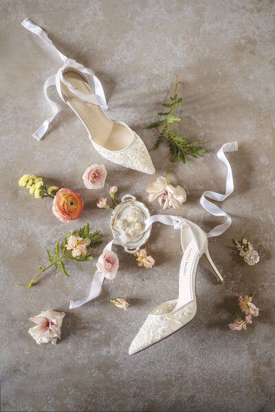 Detail of Badgley Mischka satin blue embelished shoes on a golden tray with adorned with blue petais and a thistle flower.
