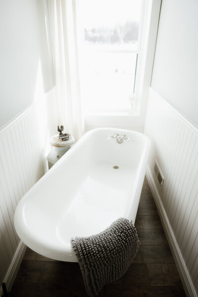 Bright and airy bathroom with a white clawfoot soaking tub, cozy knit towel, and natural light at Bear Ridge Destination.

