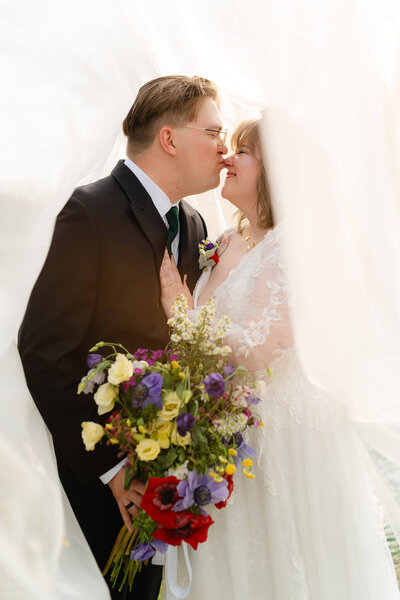 groom kissing his wife's nose playfully under her wedding veil