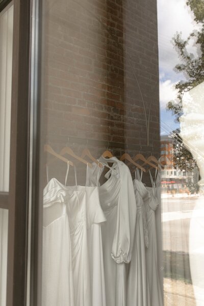 Wedding dresses on display seen through a boutique window.