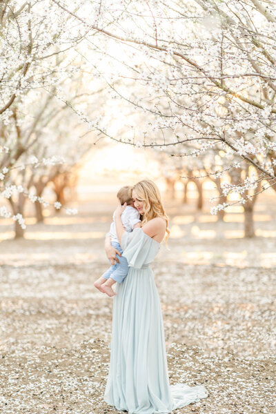 A mother embraces her son in a field of almond blossoms.