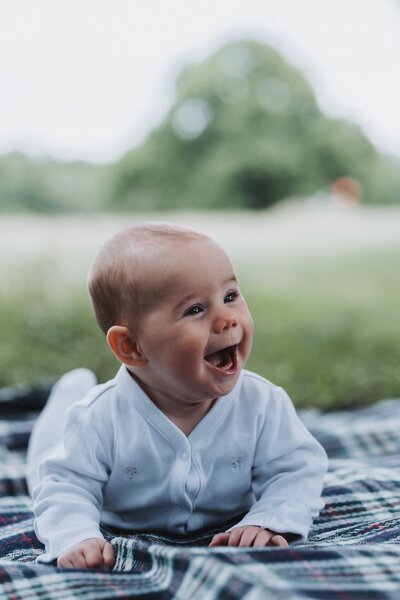 Smiling baby wearing onesie on plaid picnic blanket at the park
