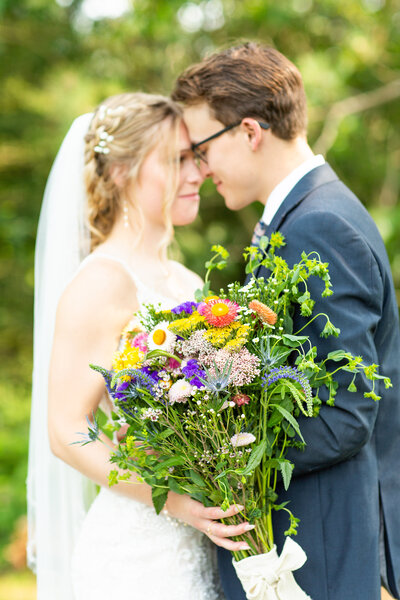 bride and groom embracing while holding a colorful flower bouquet