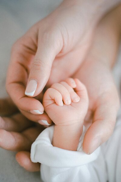 A newborn experiences the best postnatal retreat in Texas as their loving mom holds their hand with care and gratitude, showcasing the nurturing environment provided for new families.