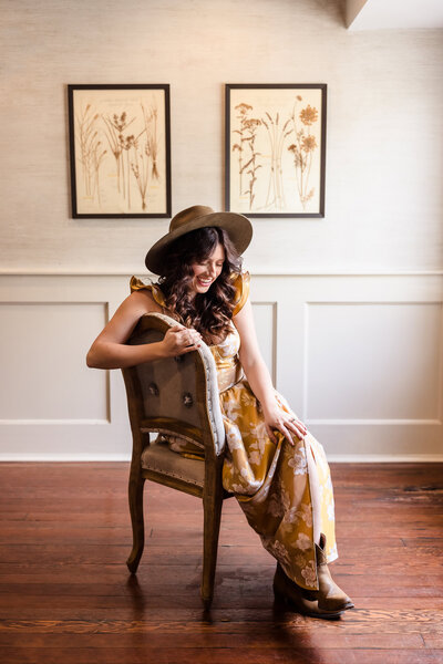 Personal branding portrait of a woman in a yellow dress and hat seated in a bright studio space, photographed in NYC.
