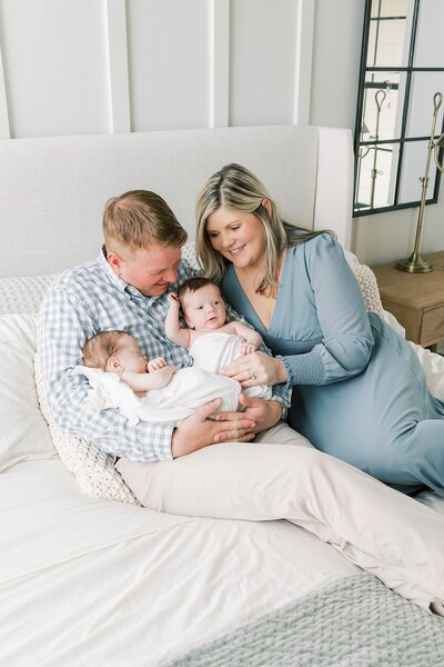 Mother and father hold their newborn twin boys in their master bedroom beautifully dressed in blue and tan tones