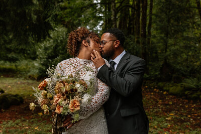 Groom gently grabs his brides face and kisses her under the towering oregon trees.