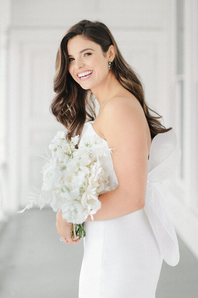 laughing bride in strapless wedding dress with bow standing on white porch with bouquet at Mattie's Austin