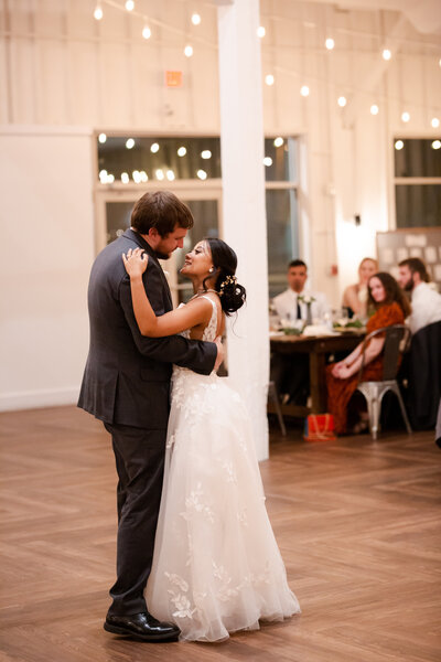 A bride and groom share their first dance in a bright reception room on the night of their wedding, photographed by Caia Grace