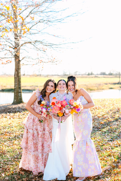 Bride posing between two bridesmaids in floral dresses holding colorful bouquets