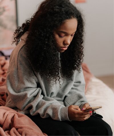 Woman sat on bed with mobile phone looking sad