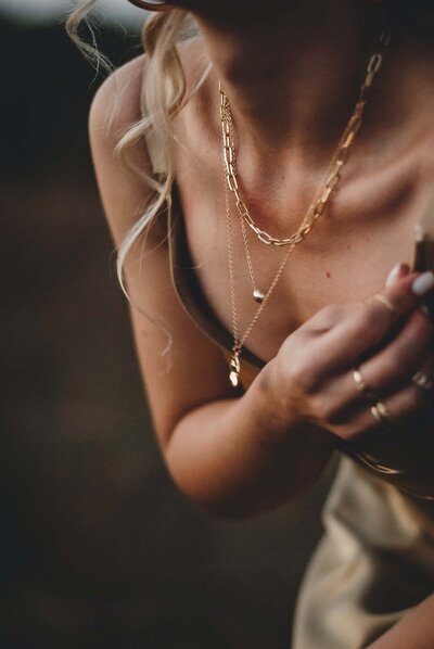 woman with multiple gold necklaces and green satin dress from neck down