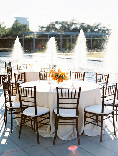 Wedding reception table with orange floral centerpiece in front of outdoor fountains