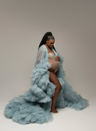 Maternity studio photo featuring a mom-to-be in a dramatic soft blue robe with train and sparkly bodysuit underneath