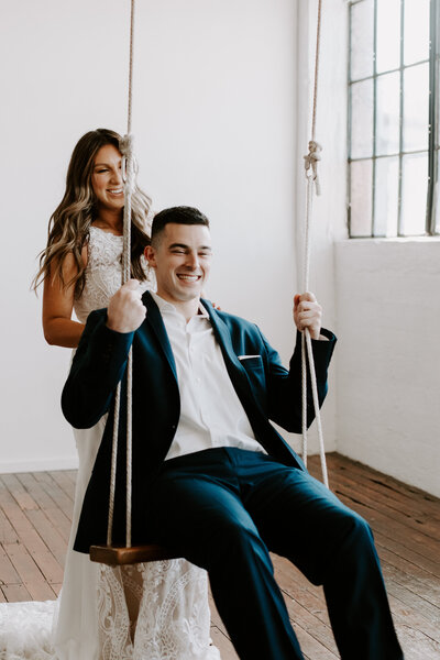 A bride pushing a groom on an indoor swing