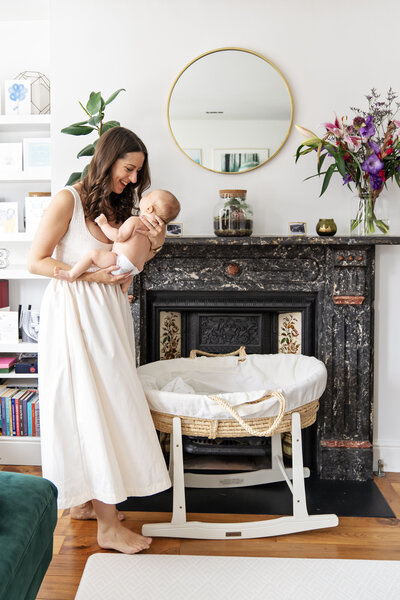 A mother holds and smiles into the eyes of her baby boy as she stands by the fireplace in her lounge by Jess Morgan Photography