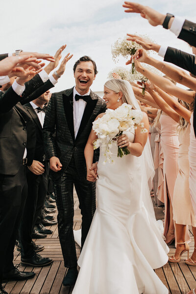 couple holding hands walking through their wedding party's arms