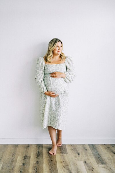 mom leaning against wall holding pregnant belly