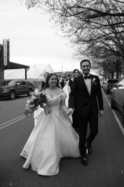Groom kissing bride’s hand during outdoor wedding, black-and-white photo.