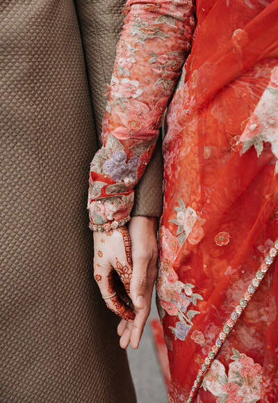 Bride in intricate red saree with henna on hands touches grooms hand