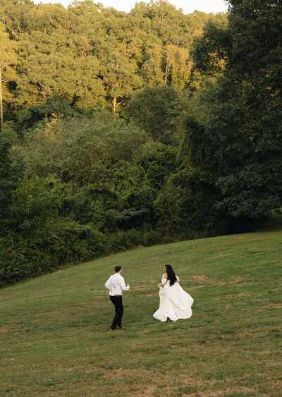 bride and groom run around on a hill surrounded by trees