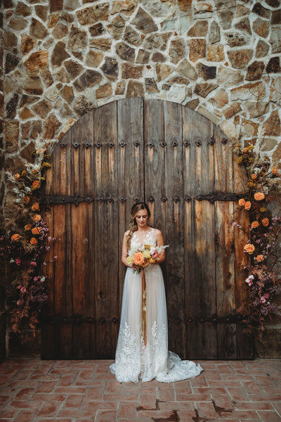 Bride holds spring bouquet and stands in front of wooden doors