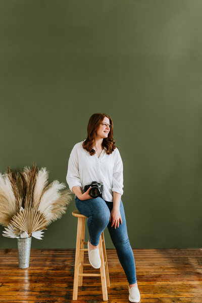 Photo of woman sitting on stool with green backdrop