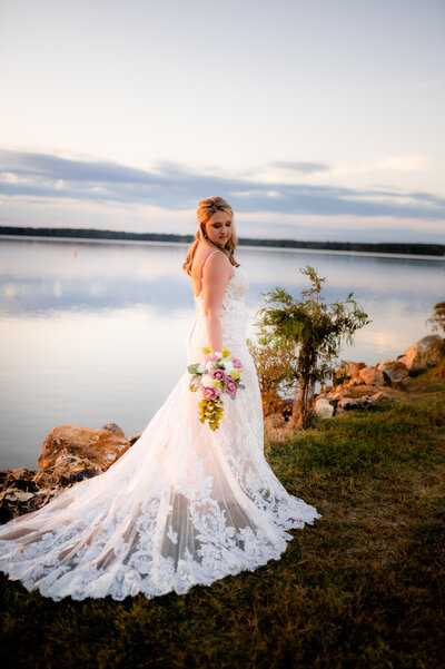 little rocck wedding photographers captures bride at sunset standing next to the water as she holds her bouquet and looks over her shoulder