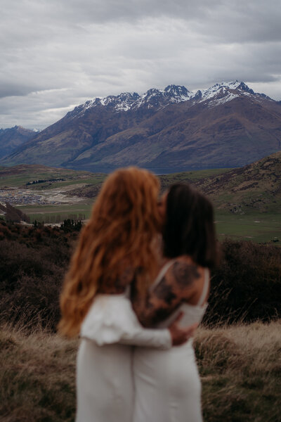 couple embracing during intimate elopement in auckland with mountains in the background