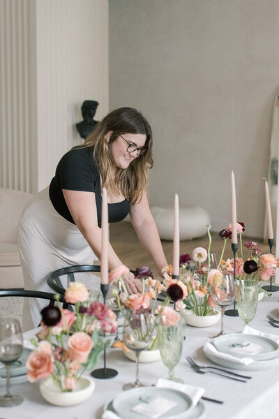 Wedding planner, Zelie & Co., setting a wedding table decorated with pink taper candles and rose arrangements 