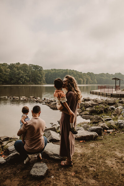 Two parents next to a lake each holding a small child 