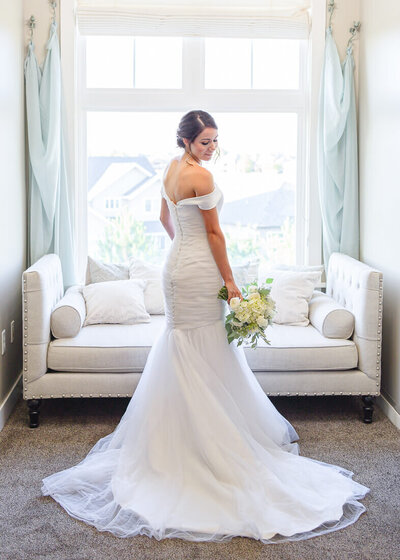 A bride in an off the shoulder white wedding dress in the brides room at the Sleepy Ridge Clubhouse, getting ready for her summer Utah wedding