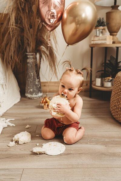 At a one year photoshoot, a little one dives into her cake smash and  takes a giant bite out of it. 
