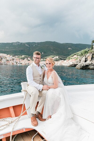 Bride and groom seated on a boat in the coastal town of Parga in the background of their destination elopement