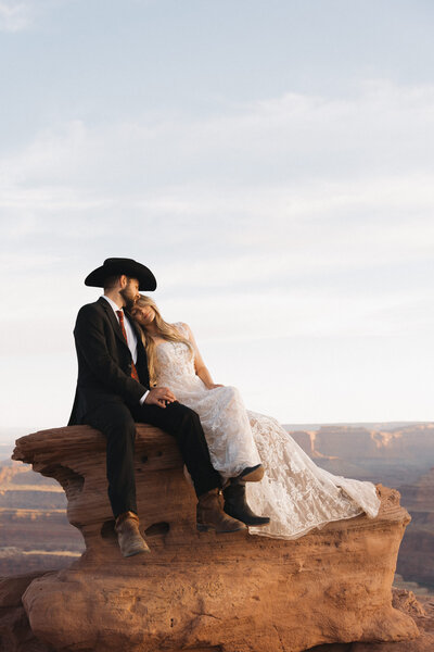 bride and groom sitting on a large red rock formation while embracing