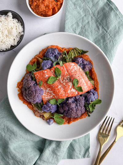 A bowl of purple cauliflower with salmon and bok choy, over a carrot-ginger purée.