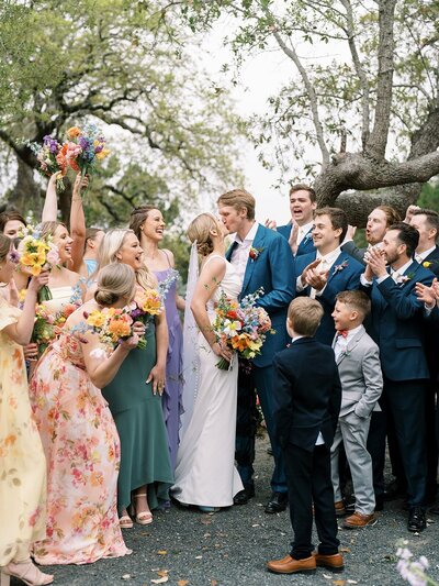Bride and groom kiss while their wedding party cheers around them, a joyful moment planned by an Austin TX wedding planner.