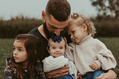A  candid moment captured between a father and his three daughters during a family photo session with Ocean Drive Photography