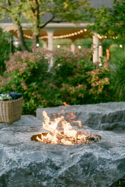 stone firepit nestled in the edge of a garden with string lights