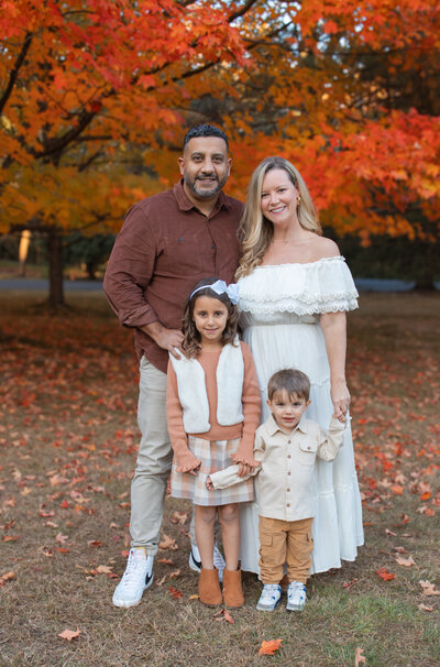 Family dressed in coordinating outfits posing under orange autumn trees.