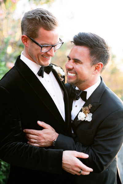 Gay couple embraces in laughter in tuxedos on their wedding day